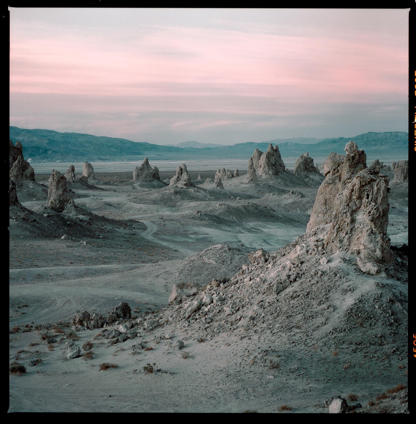 A desert landscape features numerous tufa towers under a pink and blue sky.