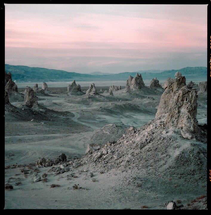 A desert landscape features numerous tufa towers under a pink and blue sky.
