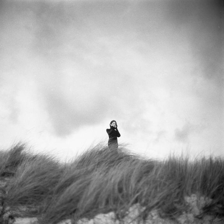 A woman stands on a grassy dune under a cloudy sky.