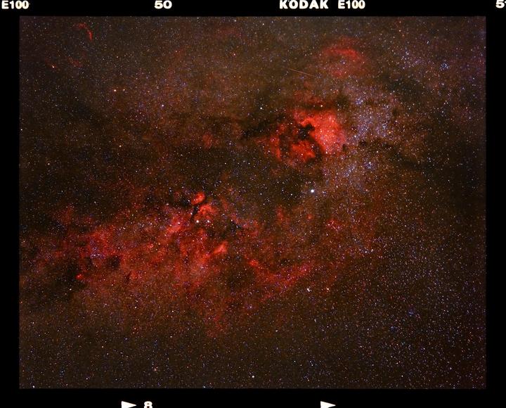 A dark sky is filled with countless stars and red interstellar hydrogen clouds.