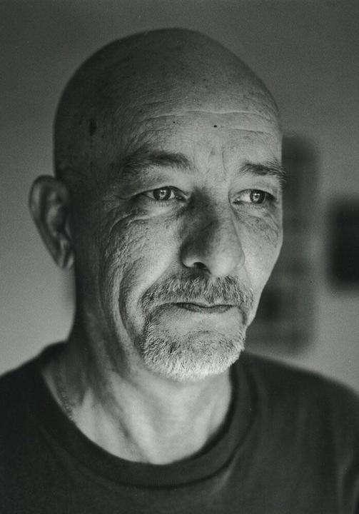 A man with a bald head and a goatee looks away from the camera.