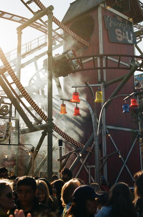 A roller coaster car is visible on a track above a crowd of people at an amusement park.