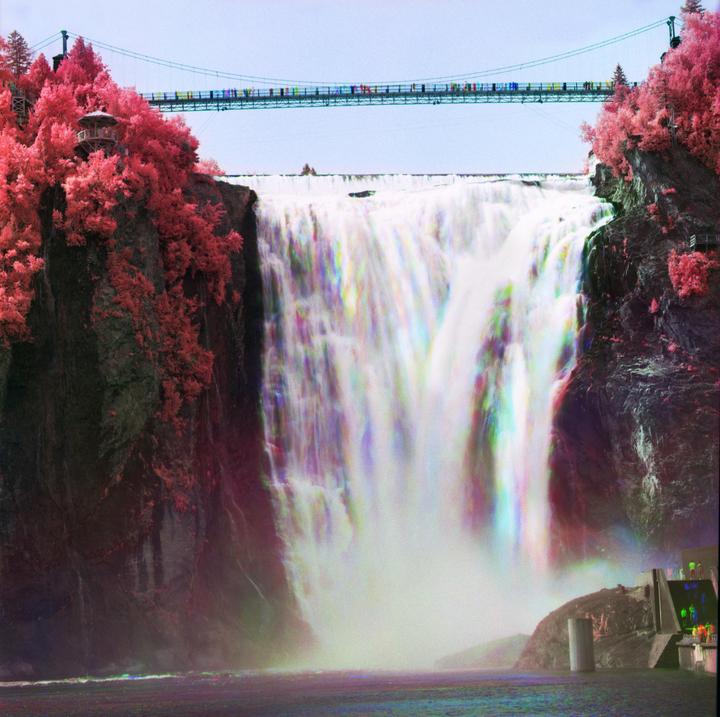 A large waterfall cascades into a body of water, with a bridge and red-leafed trees visible above.