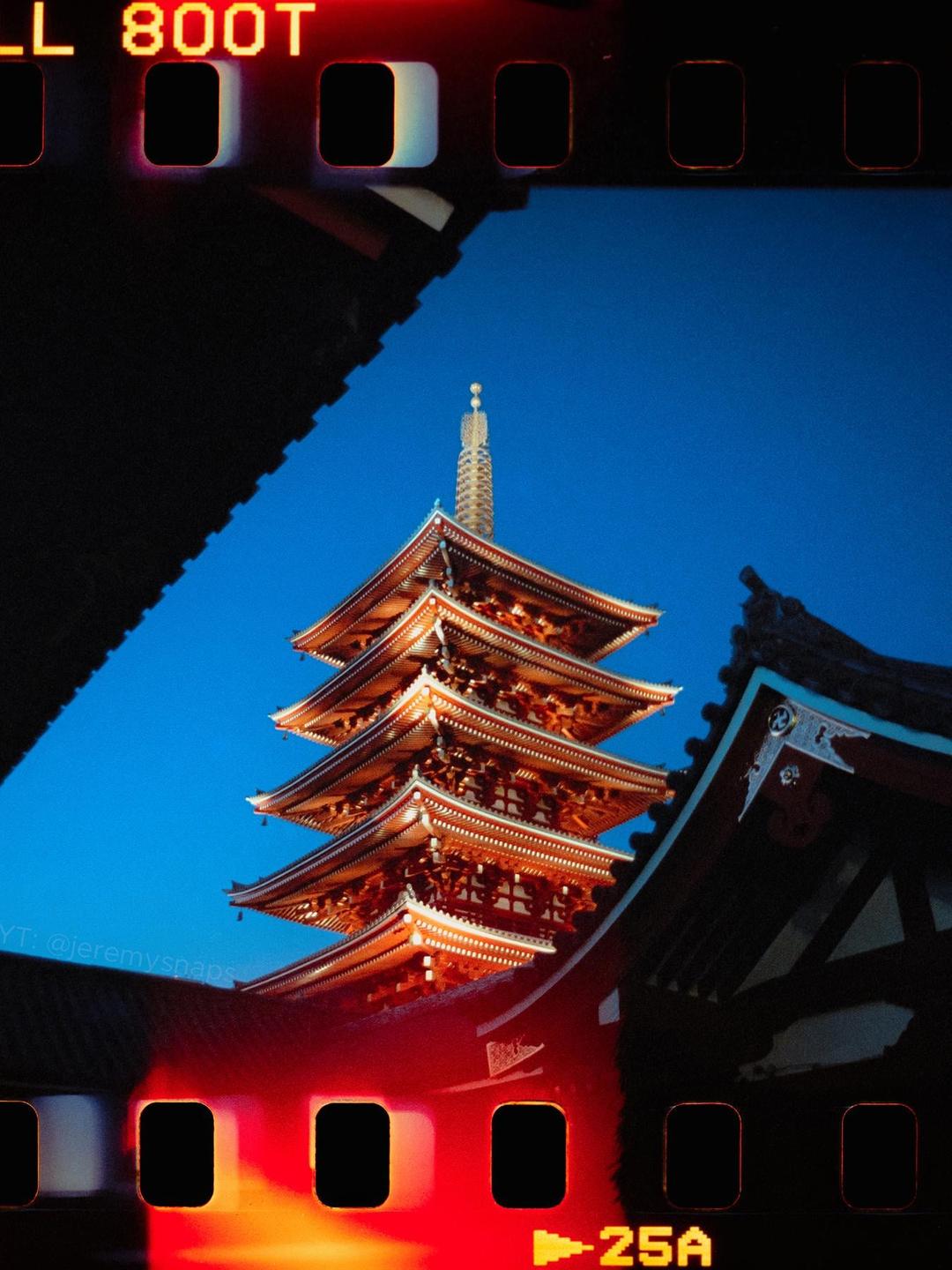 A pagoda is visible against a deep blue sky, framed by dark architectural elements and film borders.