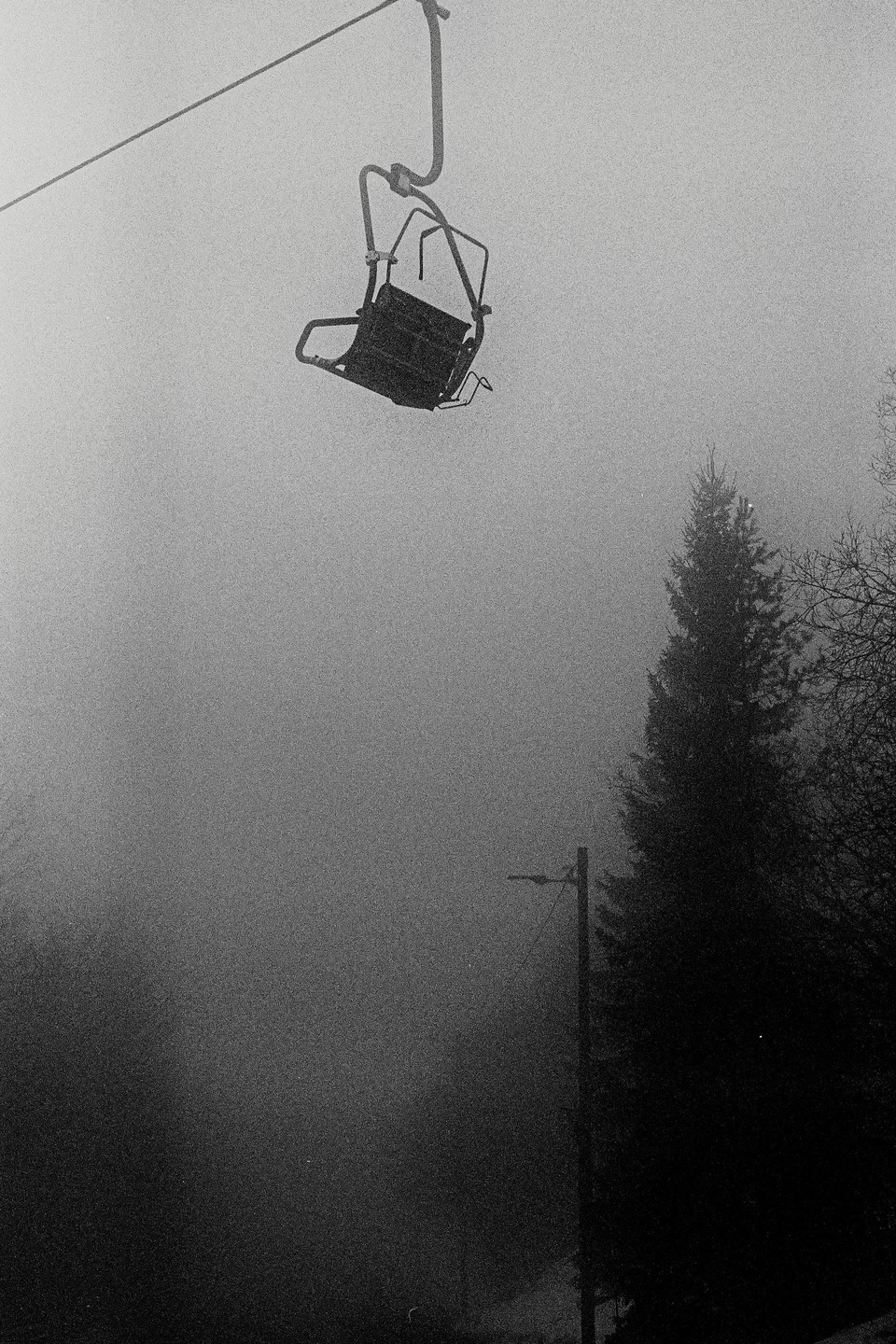 A ski lift chair hangs above a foggy landscape with trees and a utility pole.