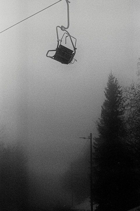 A ski lift chair hangs above a foggy landscape with trees and a utility pole.