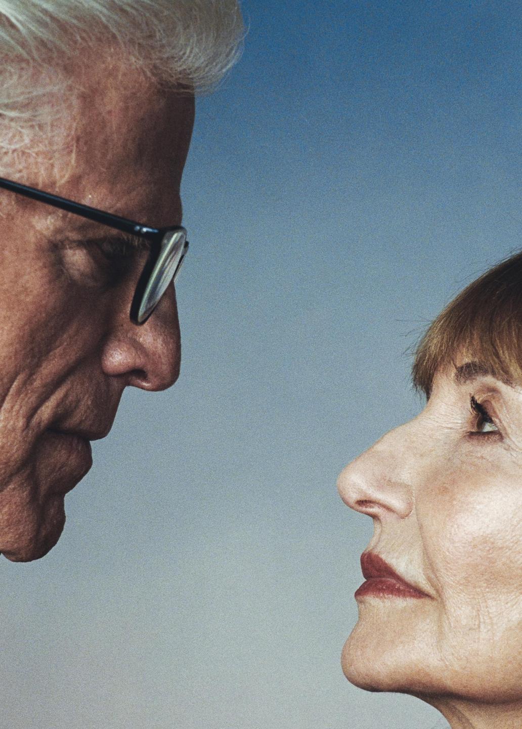 A man and a woman are looking at each other in profile against a blue background.