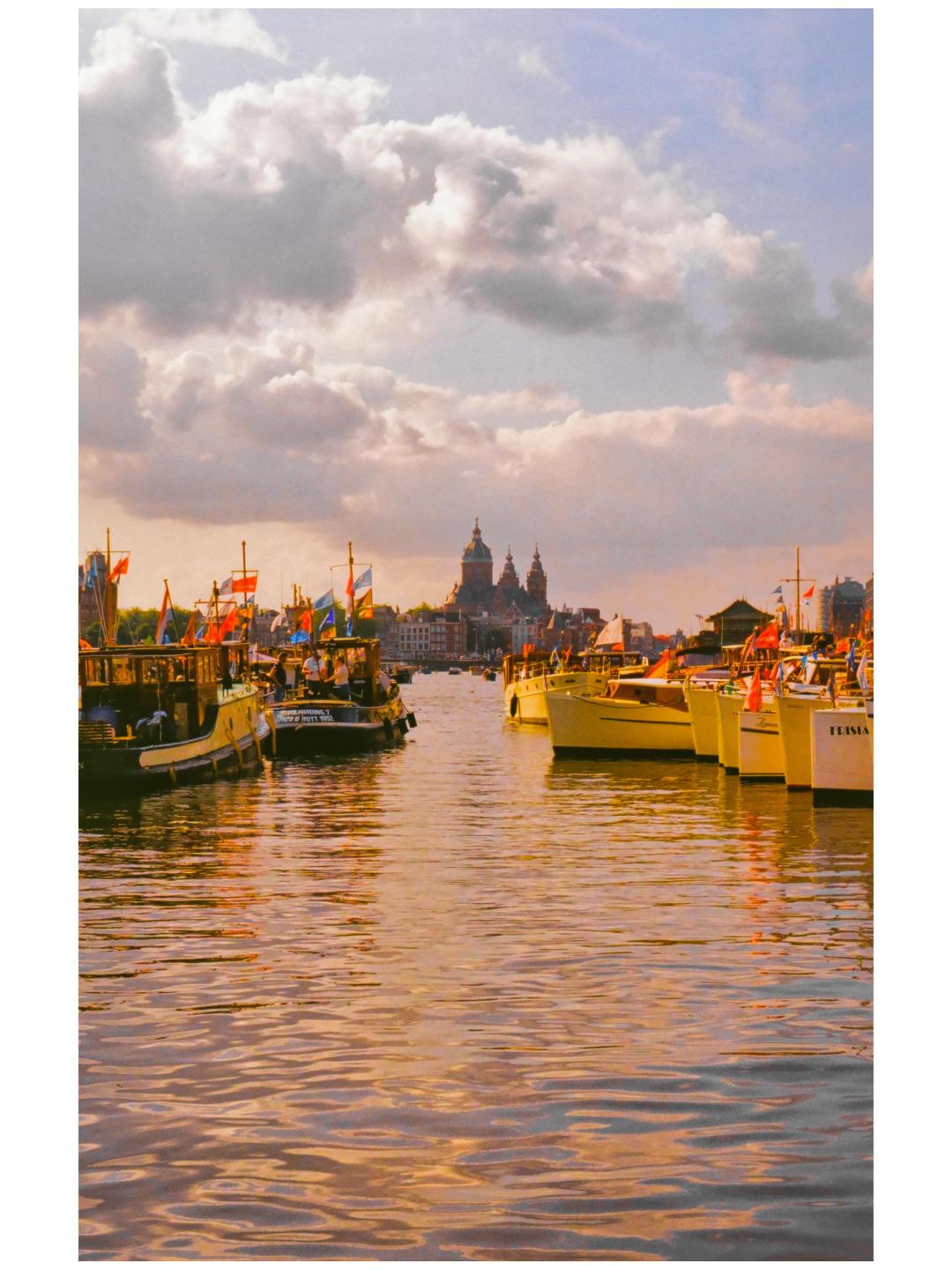 Boats are docked on a canal with a large domed building in the background under a cloudy sky.
