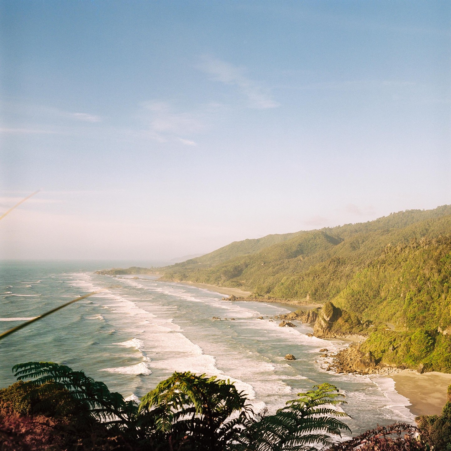 A long stretch of coastline with waves crashing on the shore is visible from a high vantage point.
