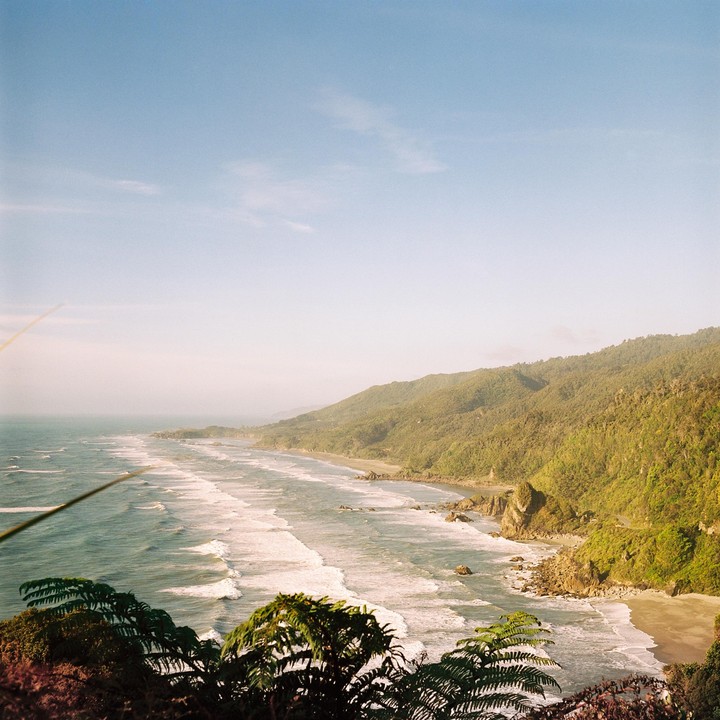 A long stretch of coastline with waves crashing on the shore is visible from a high vantage point.