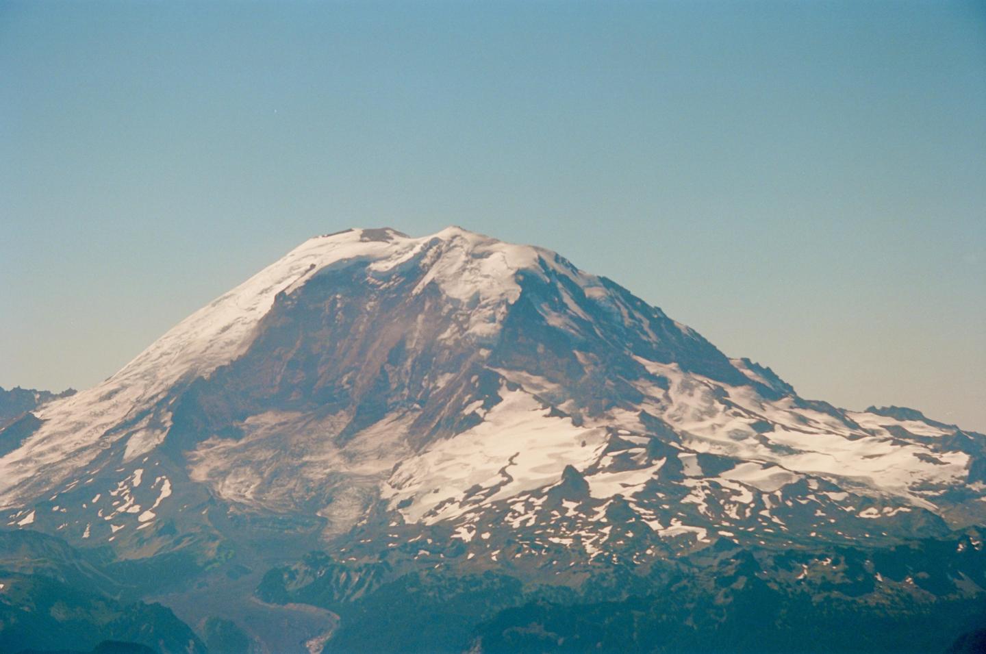 A snow-capped mountain rises majestically against a clear sky, with green foothills visible below.