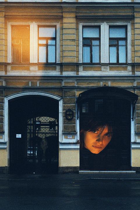 A woman's face is visible in a dark doorway next to an arched entryway in a building with windows.