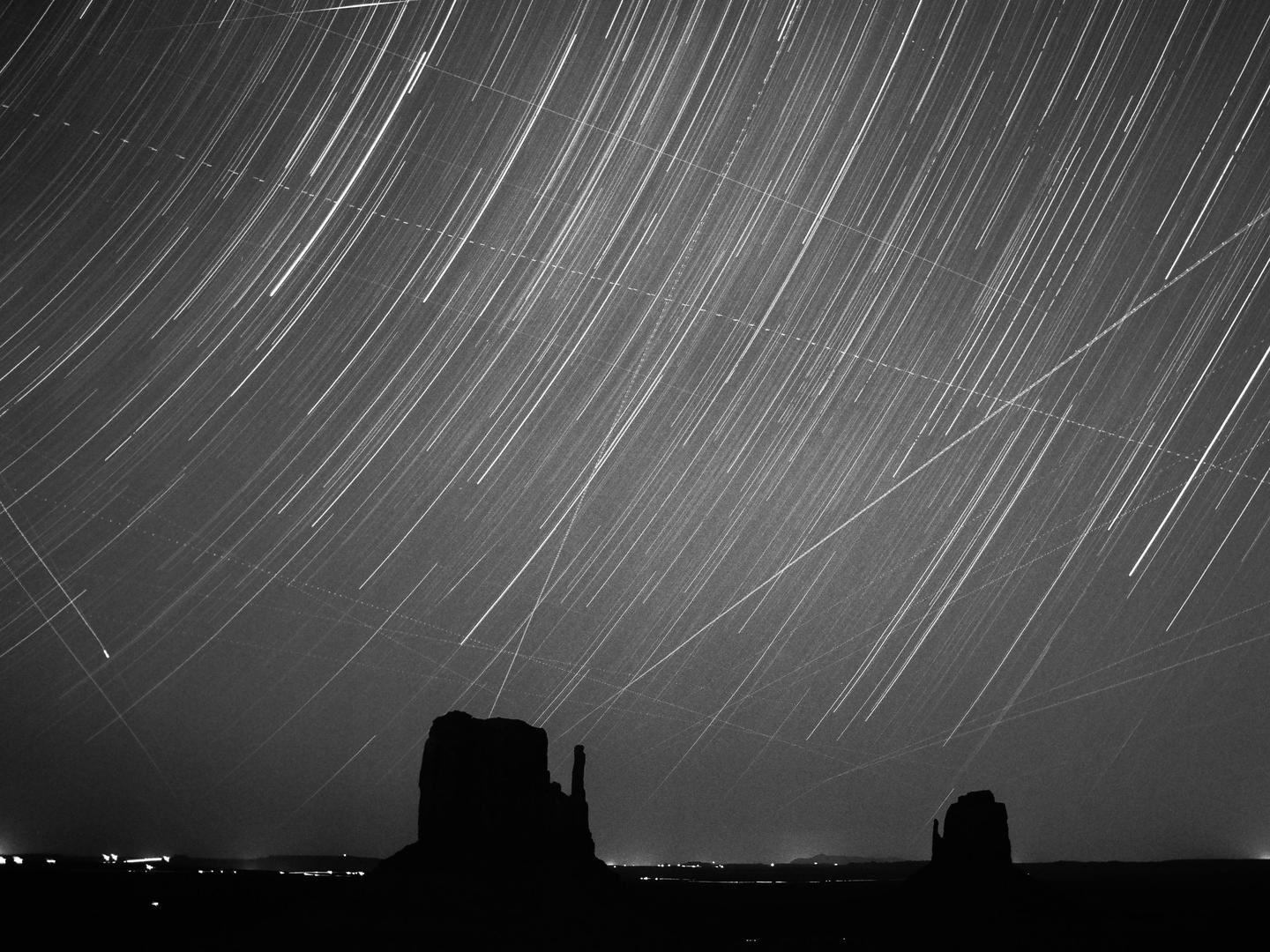A long exposure photograph shows star trails above the silhouetted rock formations of Monument Valley.