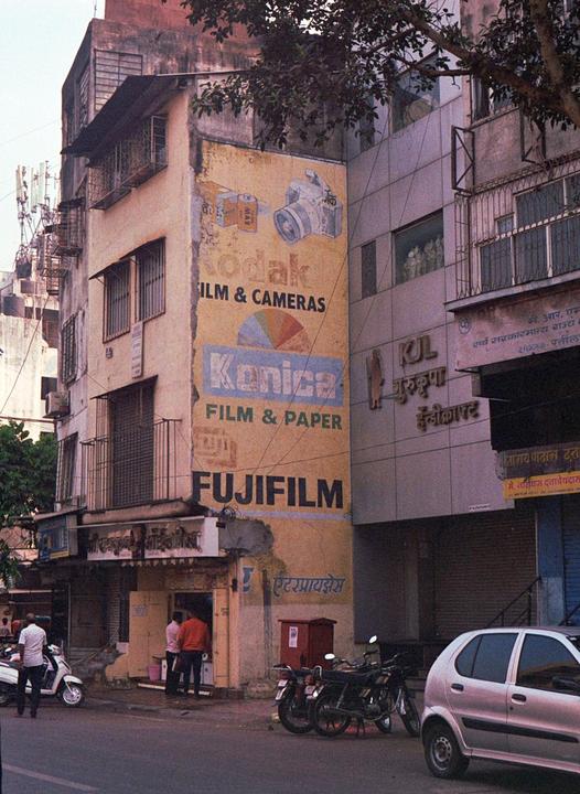 A street scene shows a building with faded advertisements for film and cameras, with people and vehicles on the street below.