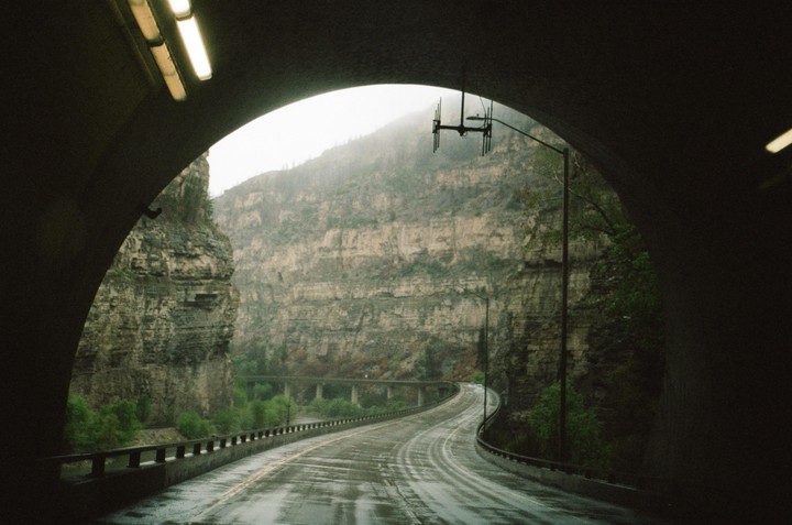 A wet road emerges from a tunnel into a canyon with steep rock walls.