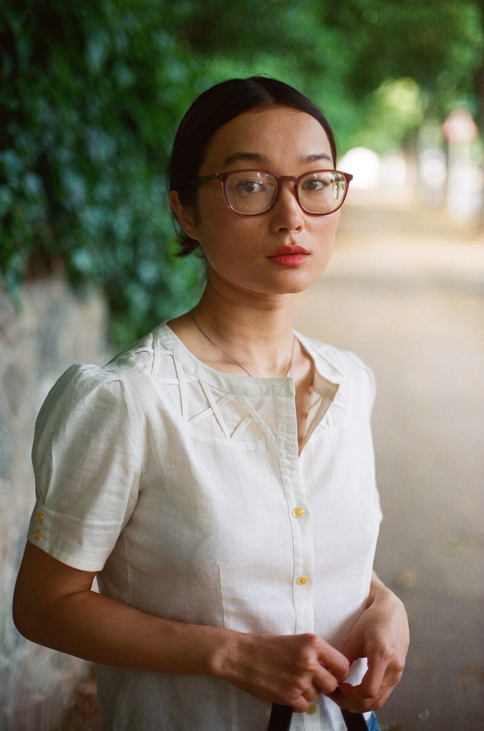 A woman with glasses and a white shirt stands outdoors looking at the viewer.