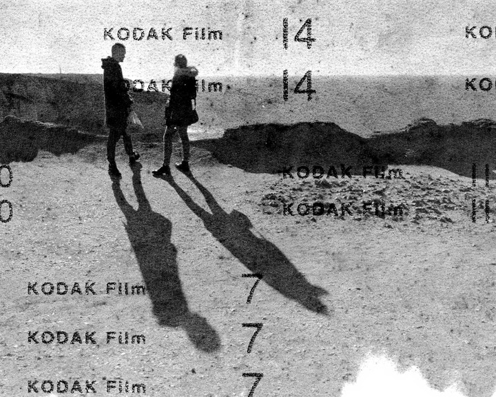 A couple stands on a textured surface with long shadows stretching out in front of them.