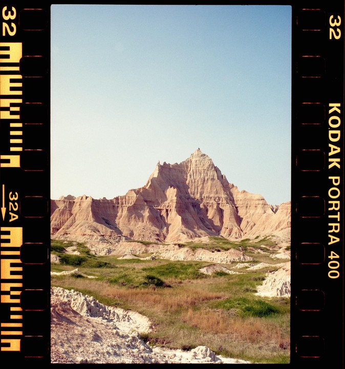A large, jagged mountain rises above a grassy plain under a clear sky.