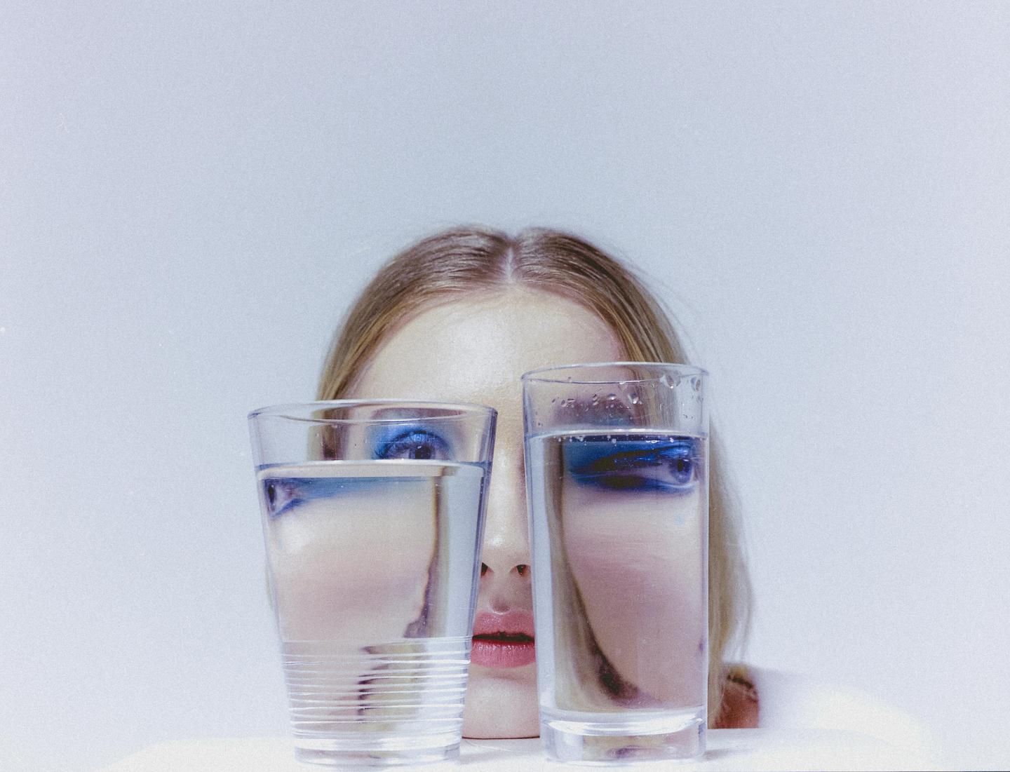 A woman with blue eyeshadow looks over two glasses of water.