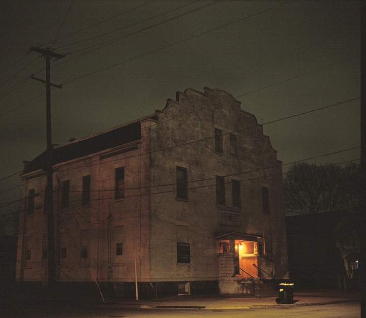 A brick building with a lit entrance stands on a street corner at night.
