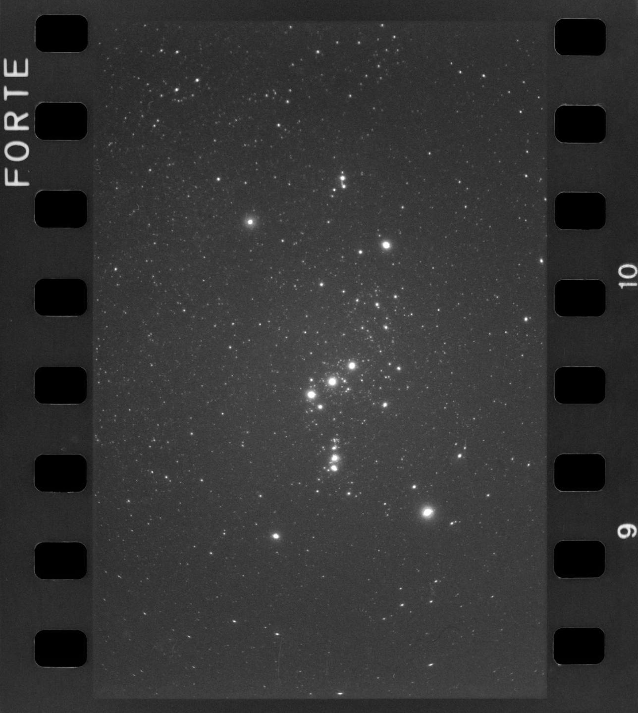 A black and white photograph shows a cluster of stars in the night sky.