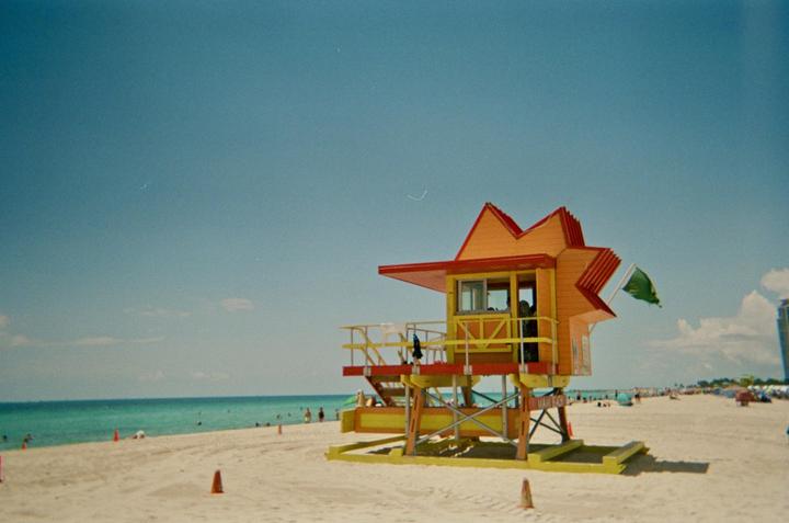 A brightly colored lifeguard stand sits on a sandy beach next to the ocean under a clear sky.