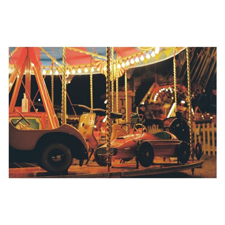 A carousel at night features a red race car, a yellow scooter, and a brown jeep.