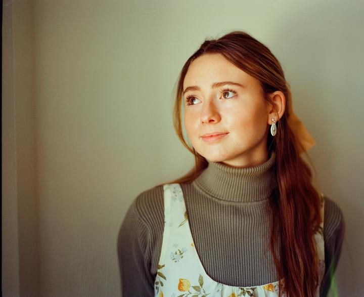 A young woman with long hair and a turtleneck looks up and to the right.