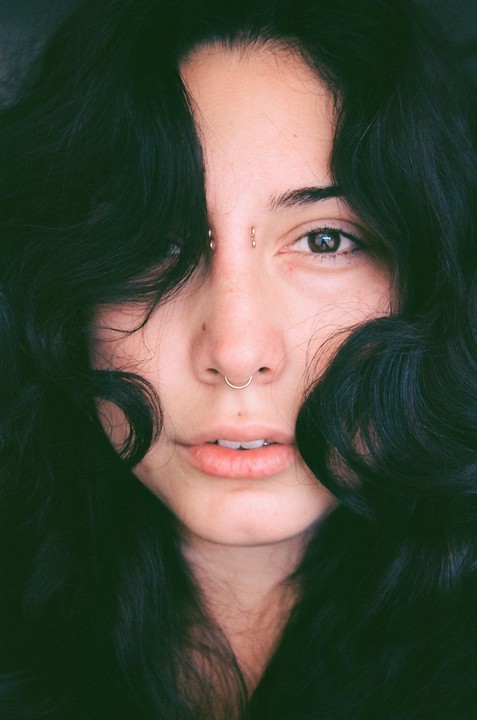A woman with dark, curly hair framing her face looks directly at the viewer.