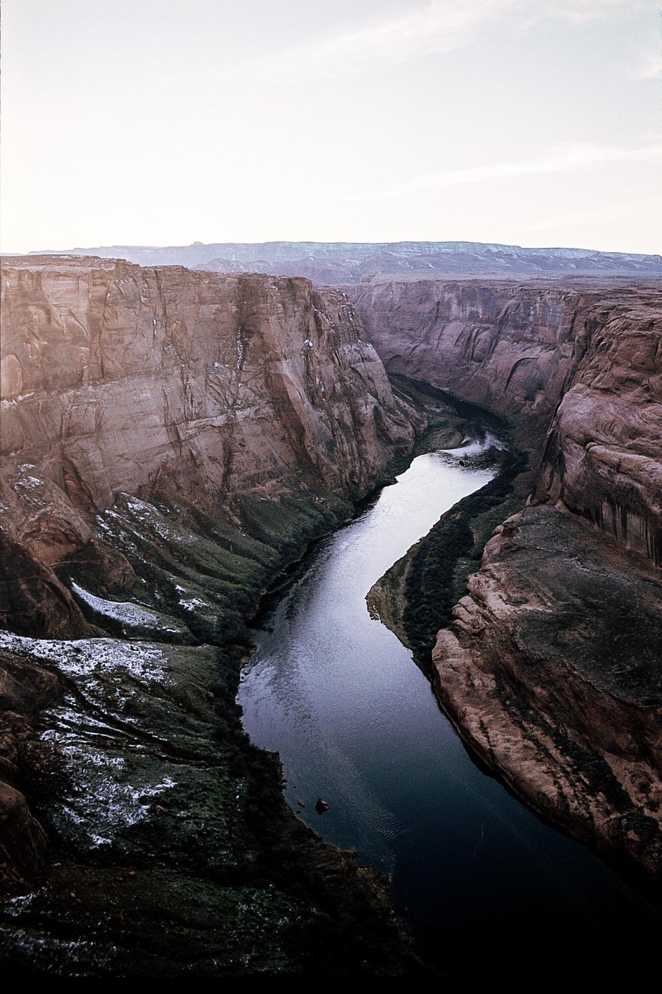 A river winds through a deep canyon with steep, rocky walls under a bright sky.