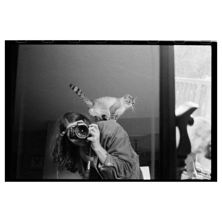 A woman takes a self-portrait in a mirror with a cat on her shoulder.