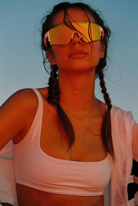 A woman with braided hair and mirrored sunglasses looks up against a blue sky.