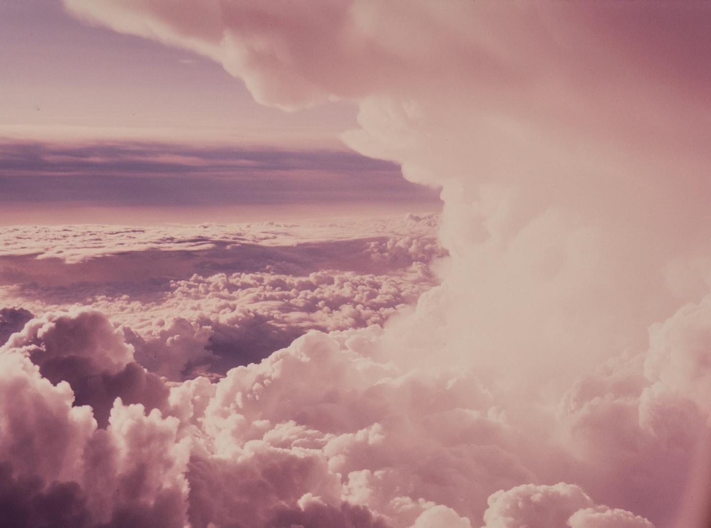 An aerial view shows a vast expanse of clouds under a sky with a purple and pink hue.