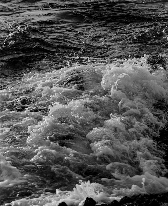 A black and white close-up shows foamy waves crashing on the shore.