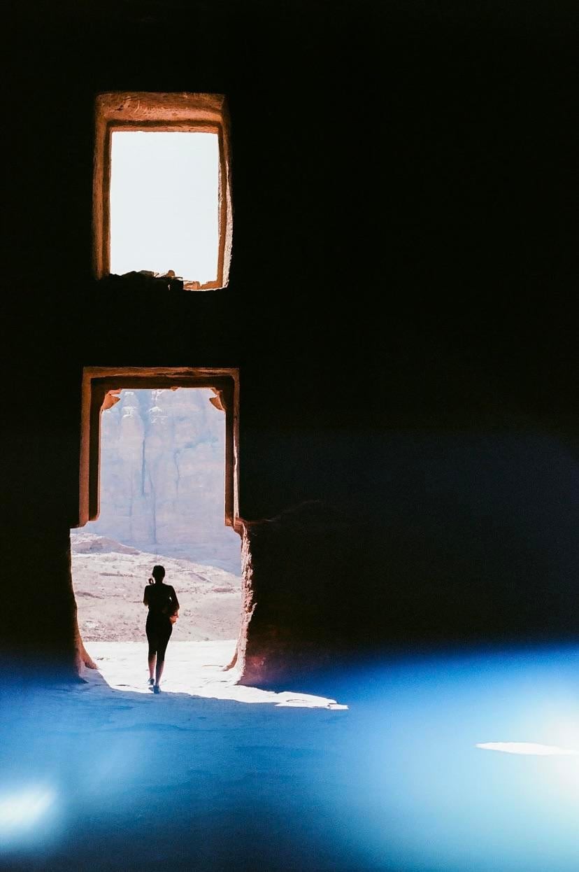 A woman stands in a doorway looking out at a desert landscape with a bright blue reflection in the foreground.