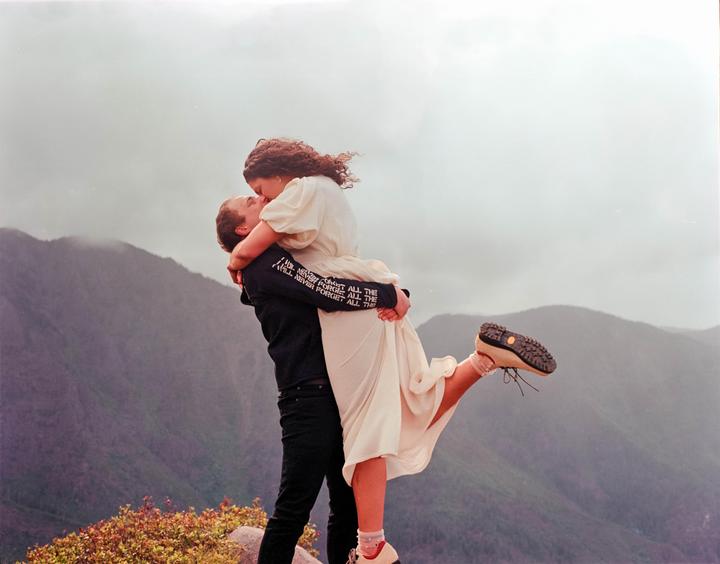 A man lifts and kisses a woman on a mountain top.