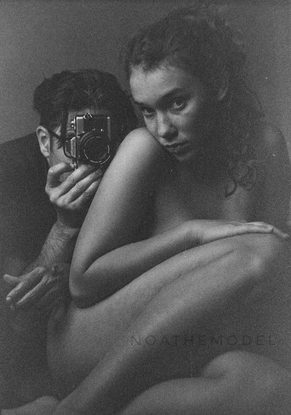 A man holds a camera to his face while a woman sits beside him looking at the viewer.