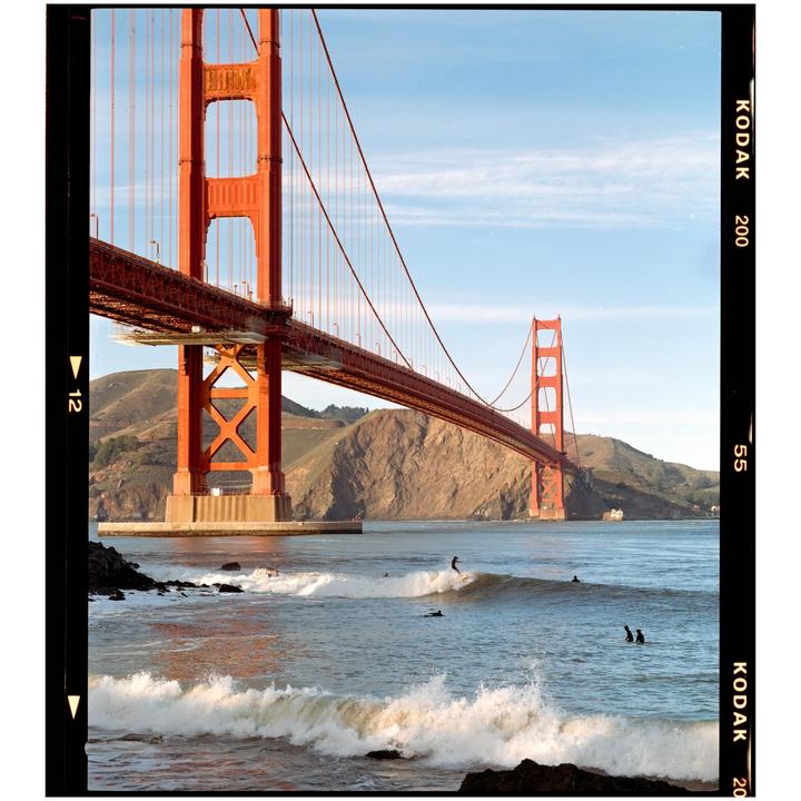 A surfer rides a wave in front of the Golden Gate Bridge.