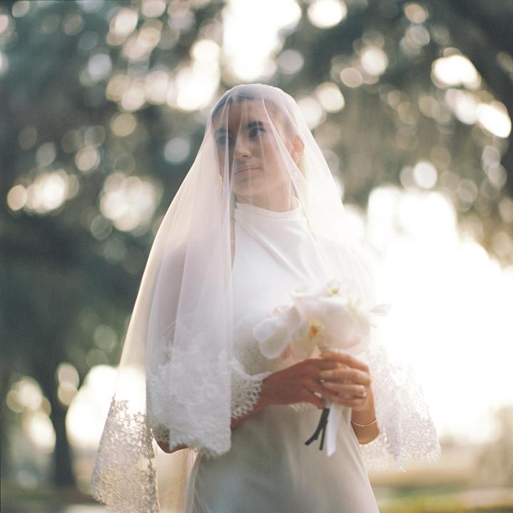 A woman in a white dress and veil holds a bouquet of white flowers.