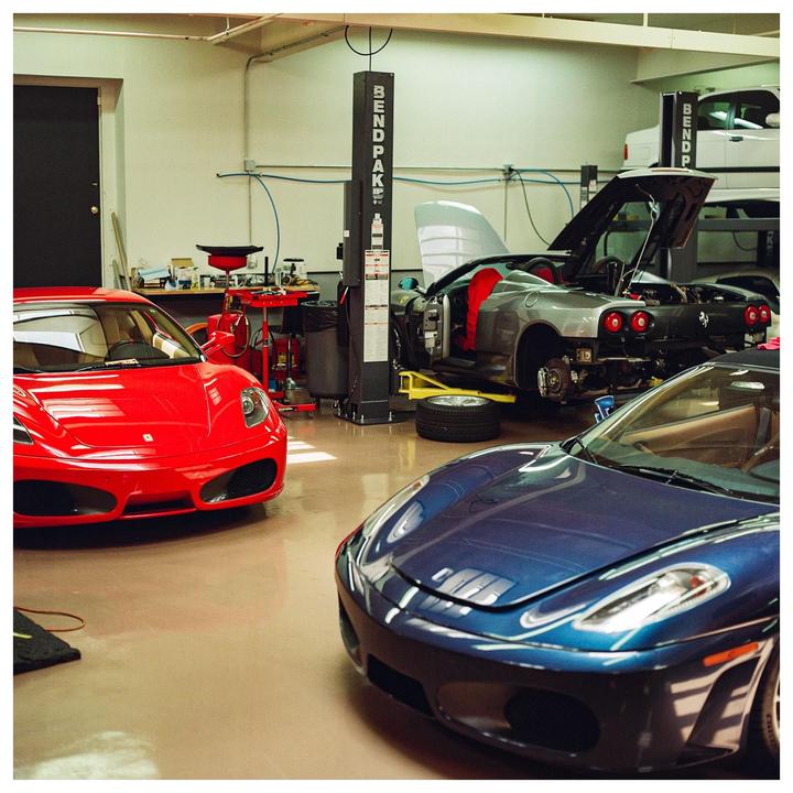 Three sports cars are parked in a garage, one of which is elevated on a lift with its engine exposed.
