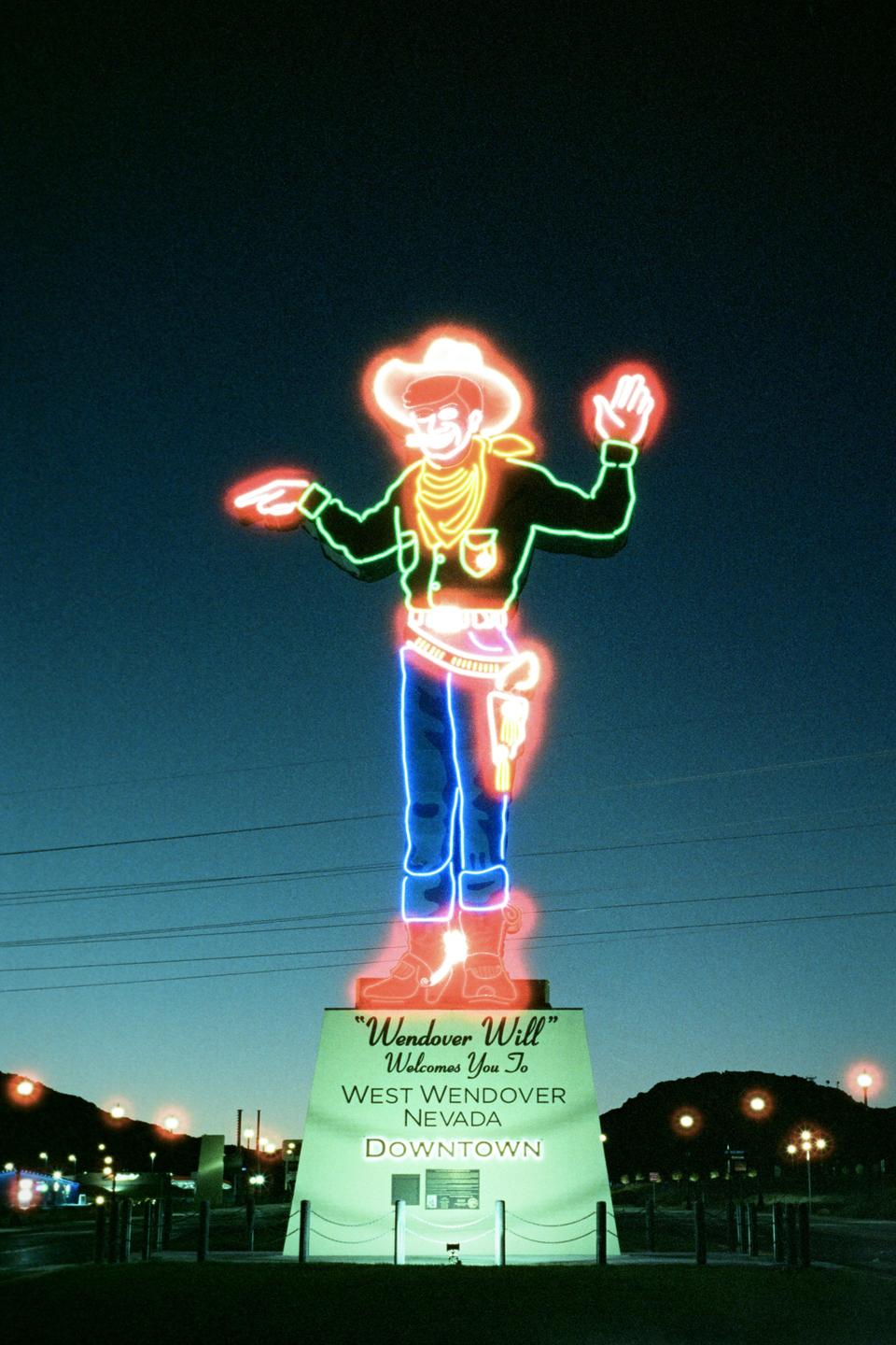 A neon sign of a cowboy stands against a dark blue sky at night.
