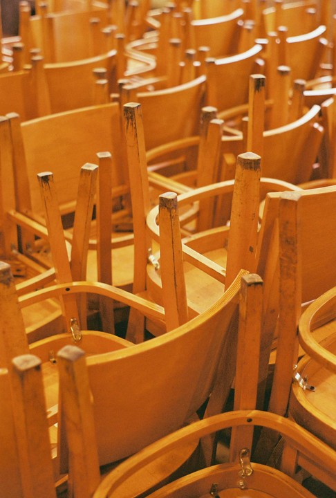 Many wooden chairs are stacked on top of each other.