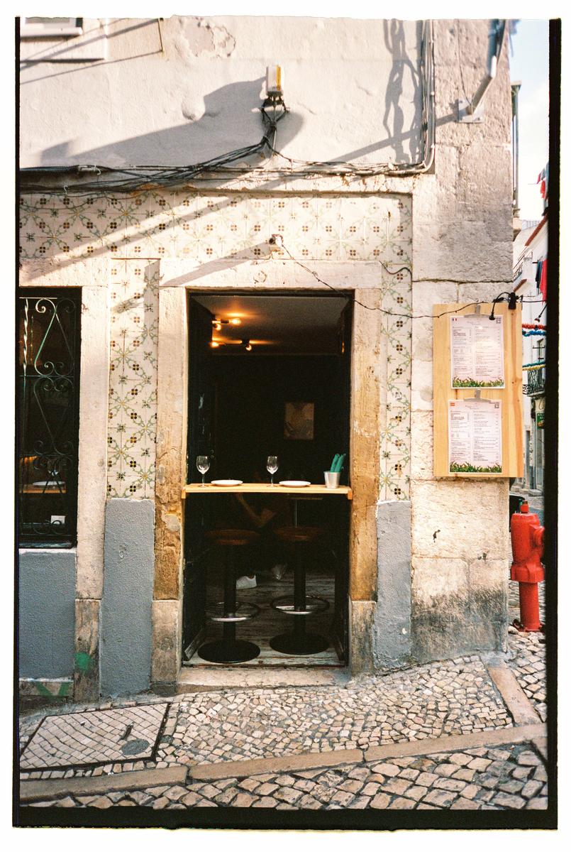 A small bar with two stools and wine glasses on a counter is visible from a cobblestone street.