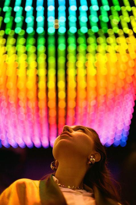 A woman looks up at a colorful display of lights.