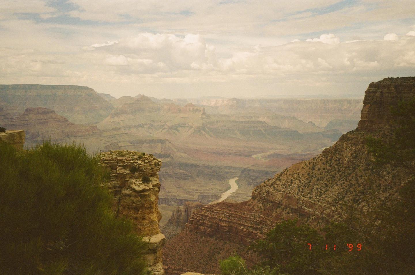 A river winds through a vast canyon under a cloudy sky.