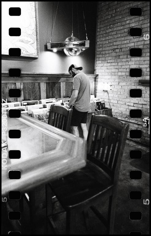 A man stands in a record store, looking through records, with a disco ball hanging above him.