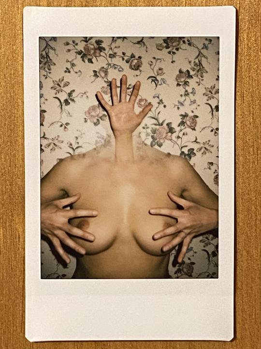 A woman's torso and hands are visible against a floral wallpaper background.