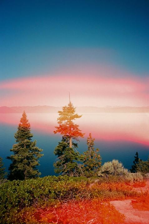 A vibrant landscape shows a lake surrounded by trees and mountains under a colorful sky.