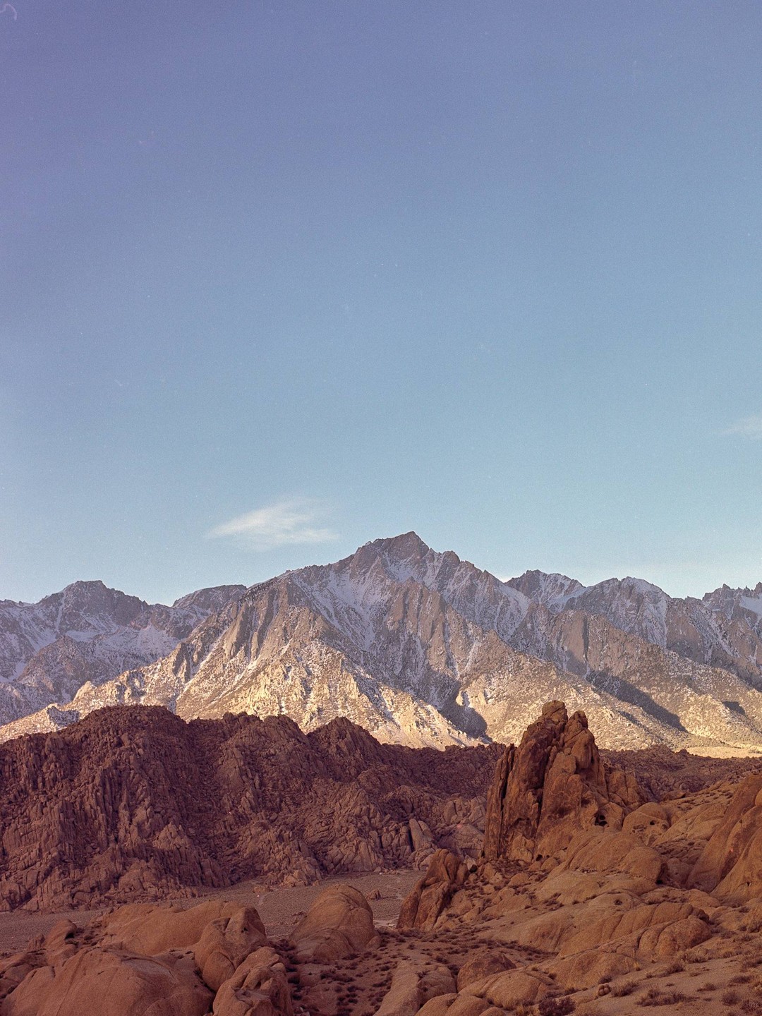 A landscape photo shows a mountain range with snow-capped peaks behind a foreground of rocky, arid hills.