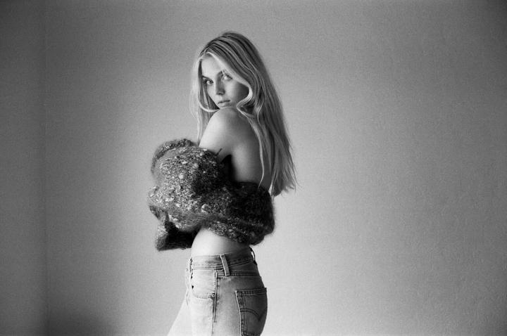 A woman with long hair and a chunky sweater looks over her shoulder.